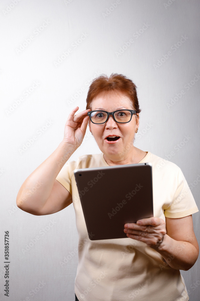 senior woman in glasses with a tablet on a white background in a light T-shirt. place for text, isolated senior woman in glasses with a tablet on a white background in a light T-shirt. place for text, isolated