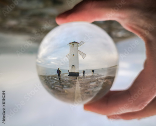 White Windmill at end of coast full of puddles near Baltic sea in Swinoujscie in reflection of crystal ball photo