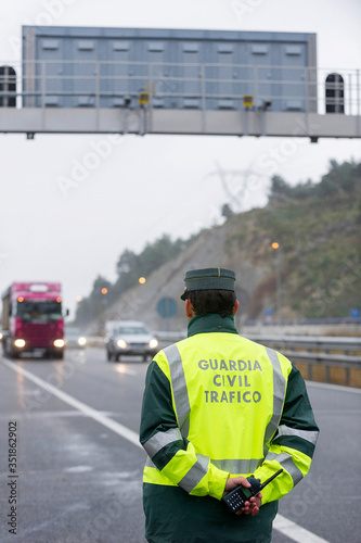 Guardia Civil officer next to a speed control monitors traffic on a highway on a rainy day