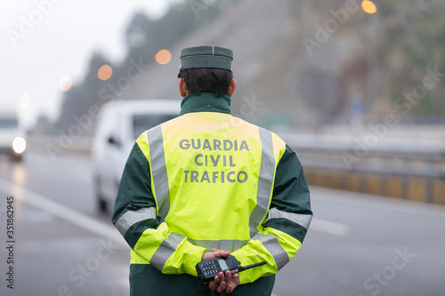 Guardia Civil officer next to a speed control monitors traffic on a highway on a rainy day