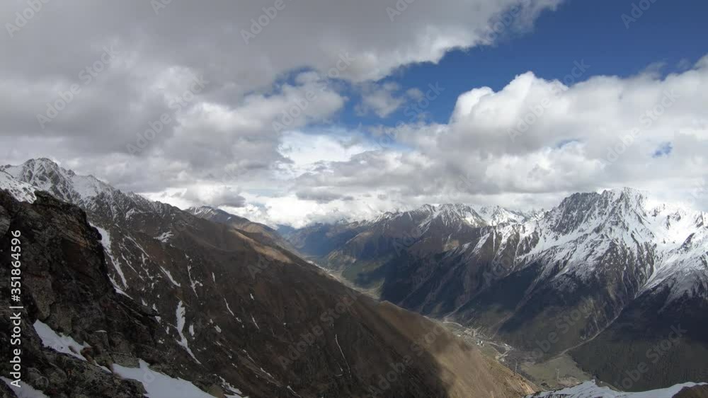 4K timelapsewide angle high above the gorge quickly float clouds covering the snow-capped peaks of high mountains. The concept of changing the weather in the mountains below the gorge village