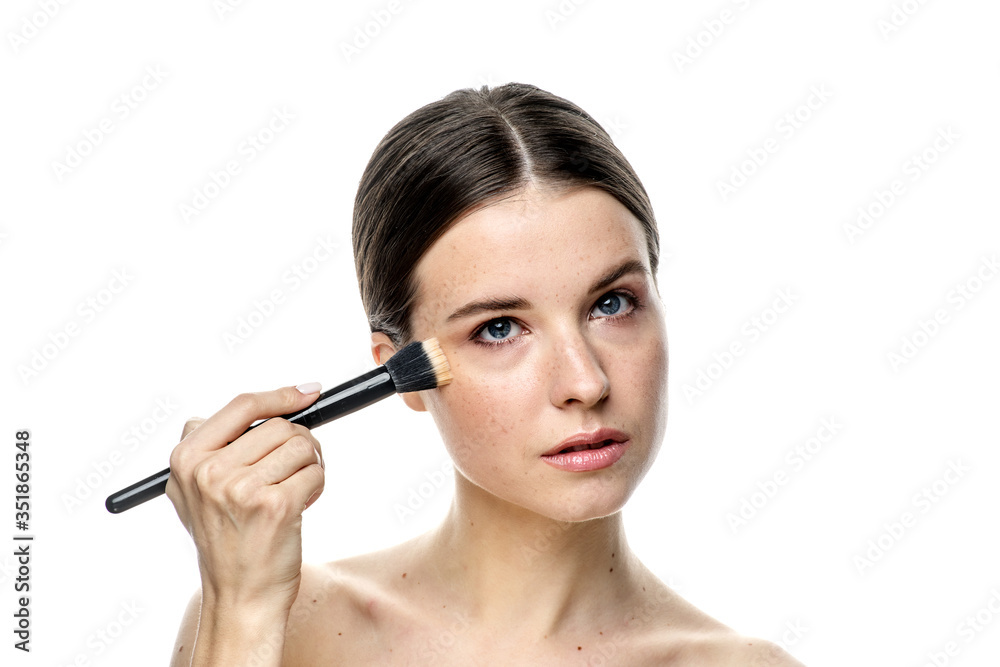close-up portrait of a girl without makeup with clean skin with a makeup brush in hand, isolated on a white background