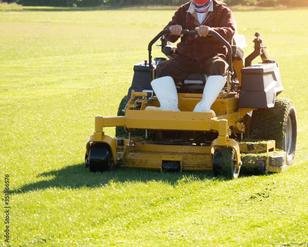Obraz premium Soft focus of Gardener use Lawn mover on green grass in the modern garden, Machine for cutting lawns, the orange sunlight splashes behind and the green background fence, mow the lawn service concept. 