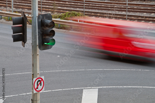 Moving blurred red car with green traffic light pole