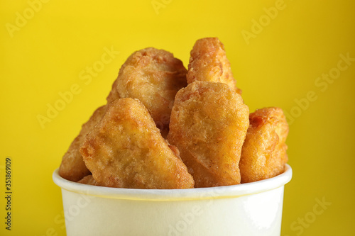 Bucket with tasty chicken nuggets on yellow background, closeup