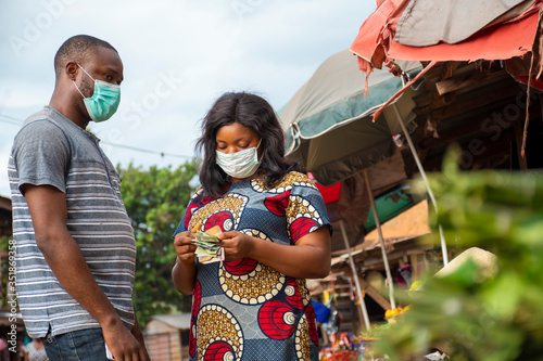 african woman selling in a local market wearing a face mask counting money from a customer