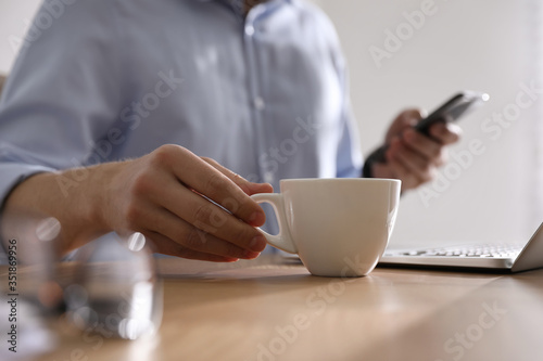 Man with cup of coffee at table indoors, closeup