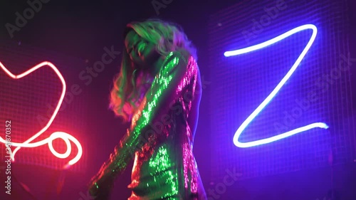 An African American woman is dancing in the neon lights of a nightclub or private party at home in a silver sequin dress with neon figure lights background. Neon concept. Prores 422. 