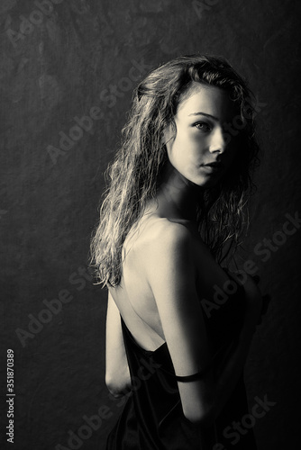 black and white portrait of a girl with long curly wet hair, bare back, turned to the side, dark shadows on the body, a mysterious portrait, textural background, portrait made in a photo studio