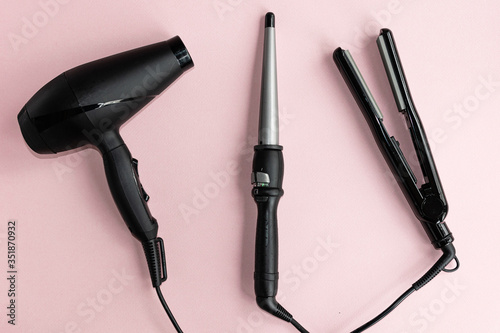 Print op canvas Black hair dryer, curling iron and hair iron on a pink background