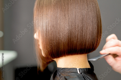 Back view of hairdresser's hand combing short hair of woman in hairdress salon.