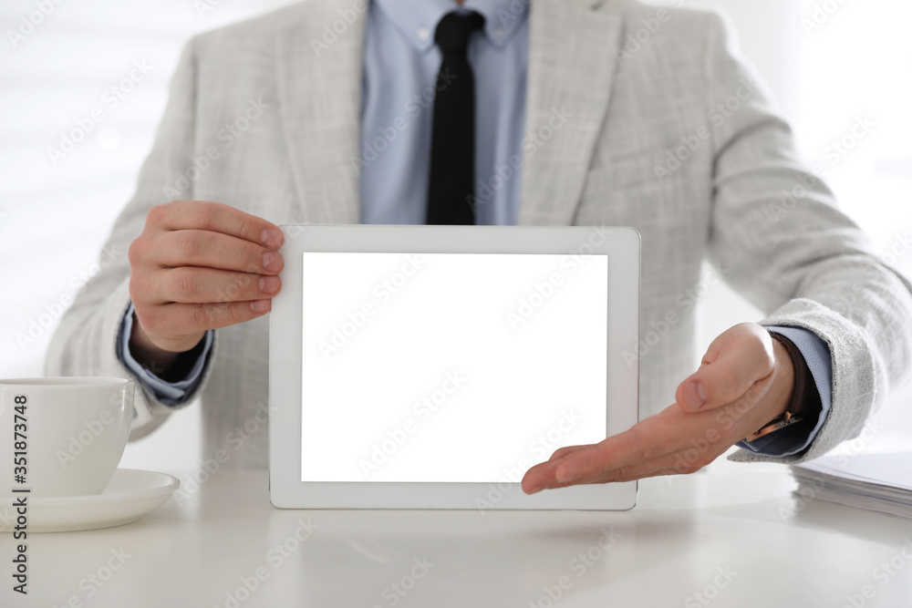 Businessman holding modern tablet with blank screen at white table in office, closeup Businessman holding modern tablet with blank screen at white table in office, closeup