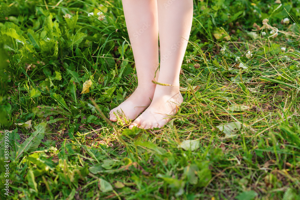 Barefoot of little child standing on a green grass in the park. Child in nature.