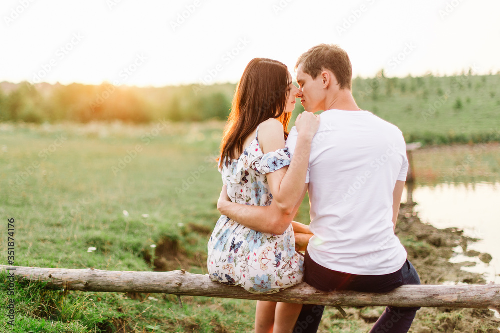 Young loving couple hug near lake sitting on log at sunset. Young loving couple hug near lake sitting on log at sunset.