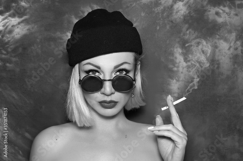 Black and white portrait of a beautiful blonde girl in a black hat with a cigarette in hand