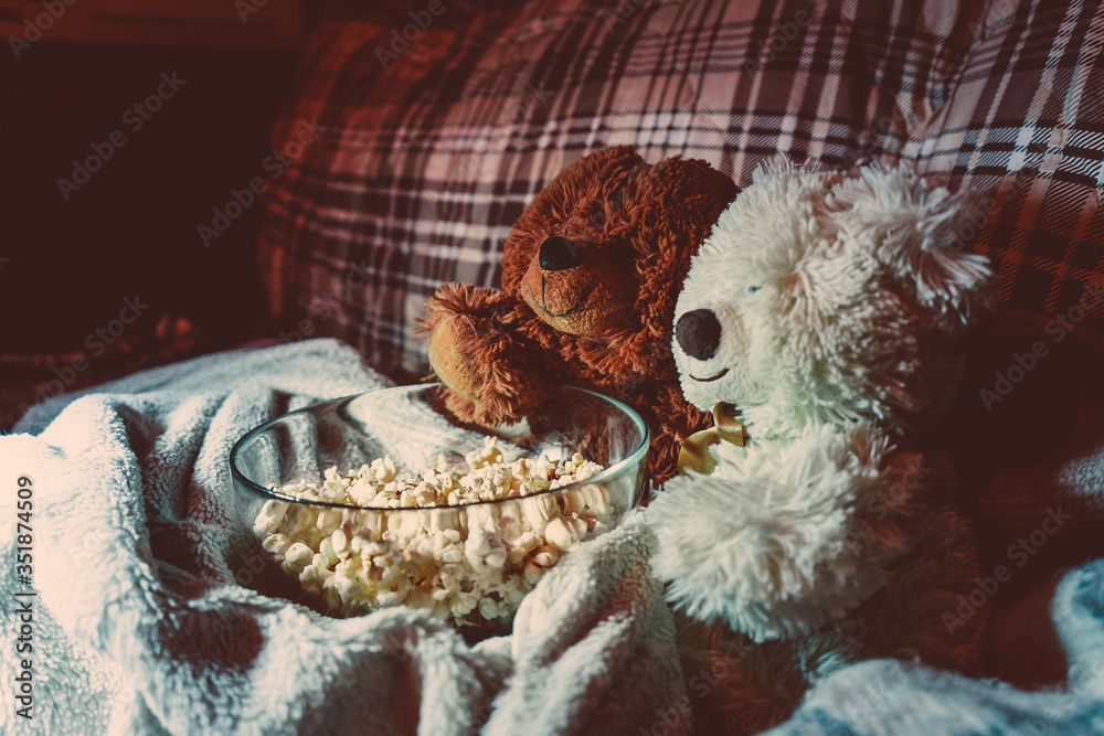 Naklejka premium A pair of amorous toy bears eat popcorn in front of the TV. Evening movie viewing with friends
