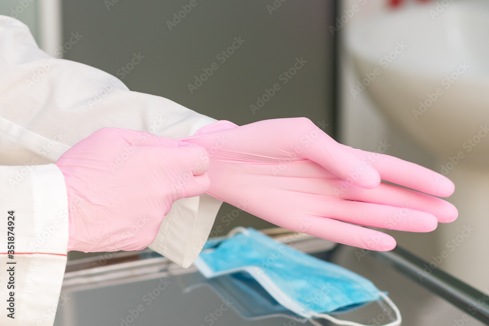 Close up of hands of doctor or nurse putting on pink protective gloves in hospital.