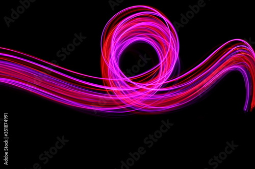 Long exposure photograph of neon colour in an abstract swirl  parallel lines pattern against a black background. Light painting photography.