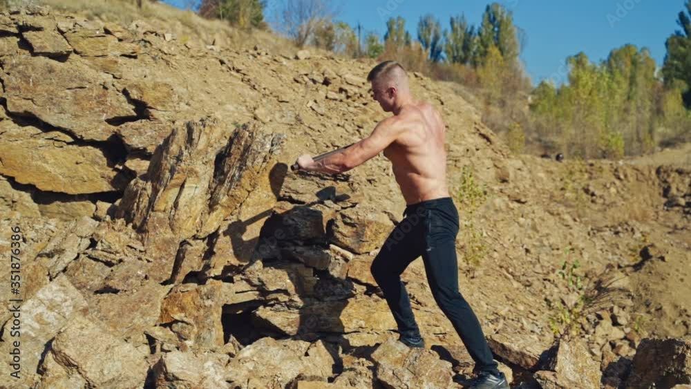 Shirtless bodybuilder splitting rocks with a sledgehammer. Strong man