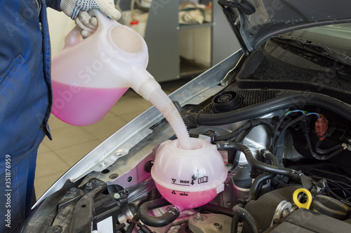 Car engine coolant expansion tank close-up. Professional mechanic pours antifreeze. photo