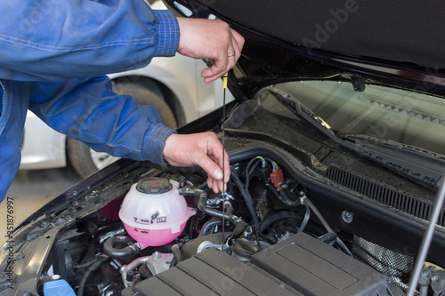 A professional mechanic is holding the oil dipstick of a car engine. Checking the engine oil level