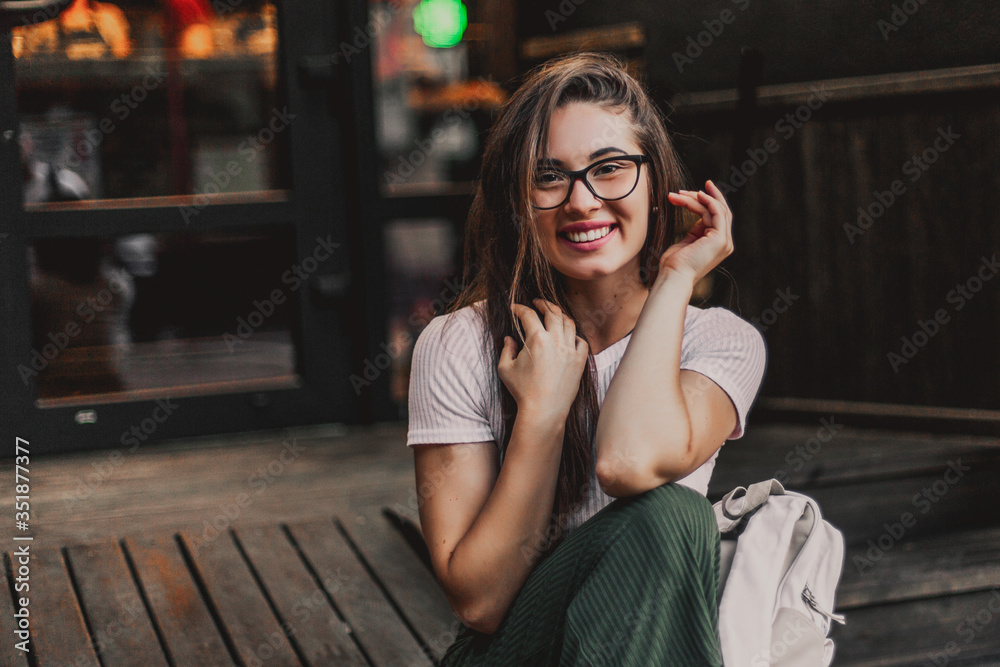 Happy smiling woman in glasses sitting on wooden steps in street.