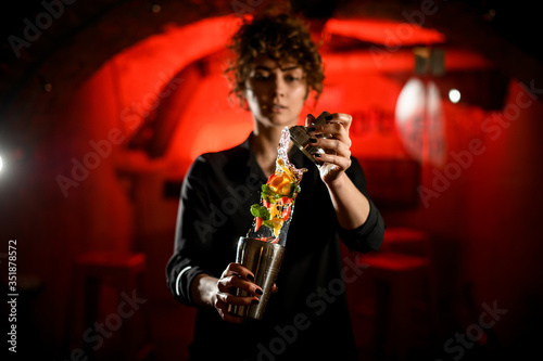 attractive woman barman neatly holds shaker with splashing drink with slices of citrus and mint