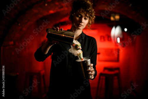 young attractive female barman pours smoky cocktail from shaker into glass