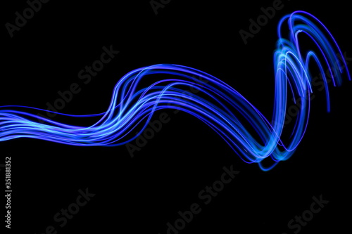 Long exposure photograph of neon blue colour in an abstract swirl, parallel lines pattern against a black background. Light painting photography.