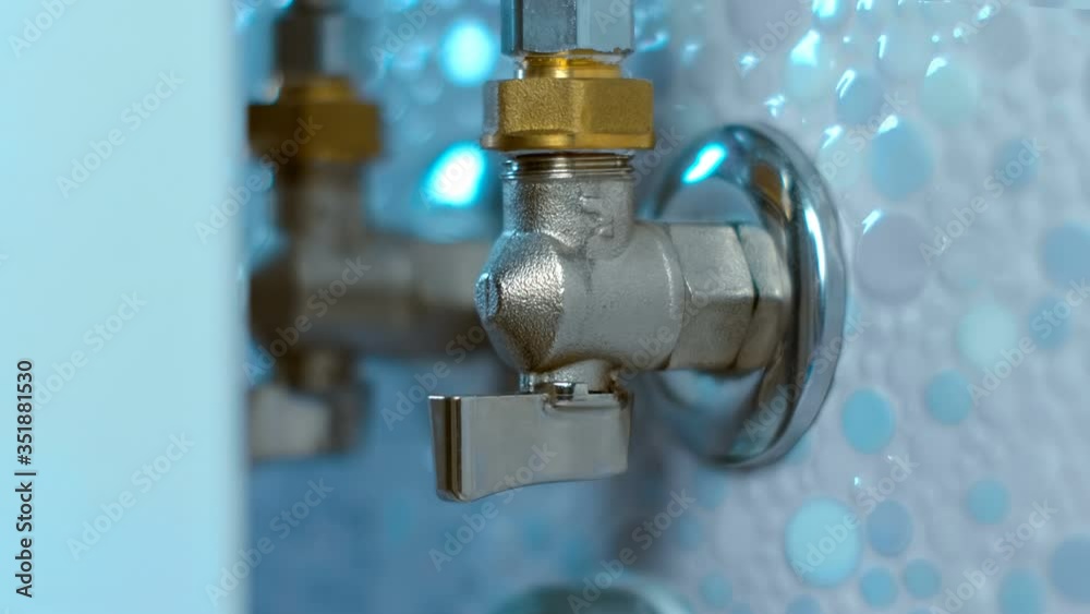 The hand opens (closes) a modern ball valve and turns on the cold (hot) water in the bathroom on the wall, tiled. Closeup. Shallow depth of field The hand opens (closes) a modern ball valve and turns on the cold (hot) water in the bathroom on the wall, tiled. Closeup. Shallow depth of field