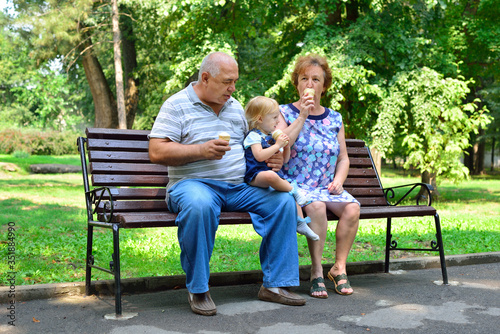 Grandmother, grandfather and granddaughter are sitting on a bench and eating ice cream