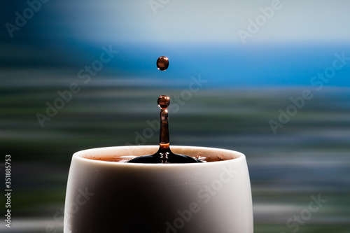 Red wine splash. Reaction of a falling drop on a red wine  surface in a completely filled white plastic cup. Studio photo with matching blue colored background. Beautiful wine drop
