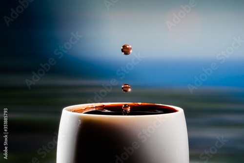 Red wine splash. Reaction of a falling drop on a red wine  surface in a completely filled white plastic cup. Studio photo with matching blue colored background. Beautiful wine drop