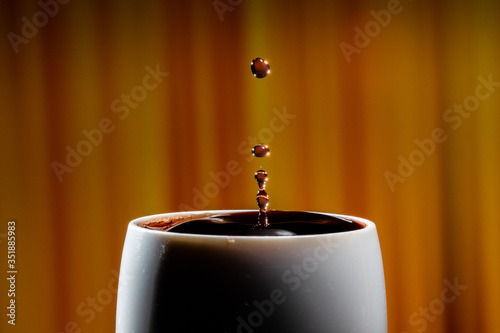 Red wine splash. Reaction of a falling drop on a red wine  surface in a completely filled white plastic cup. Studio photo with matching orange striped colored background. Beautiful wine drop.