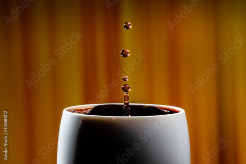 Red wine splash. Reaction of a falling drop on a red wine  surface in a completely filled white plastic cup. Studio photo with matching orange striped colored background. Beautiful wine drop.