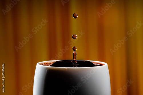 Red wine splash. Reaction of a falling drop on a red wine  surface in a completely filled white plastic cup. Studio photo with matching orange striped colored background. Beautiful wine drop.