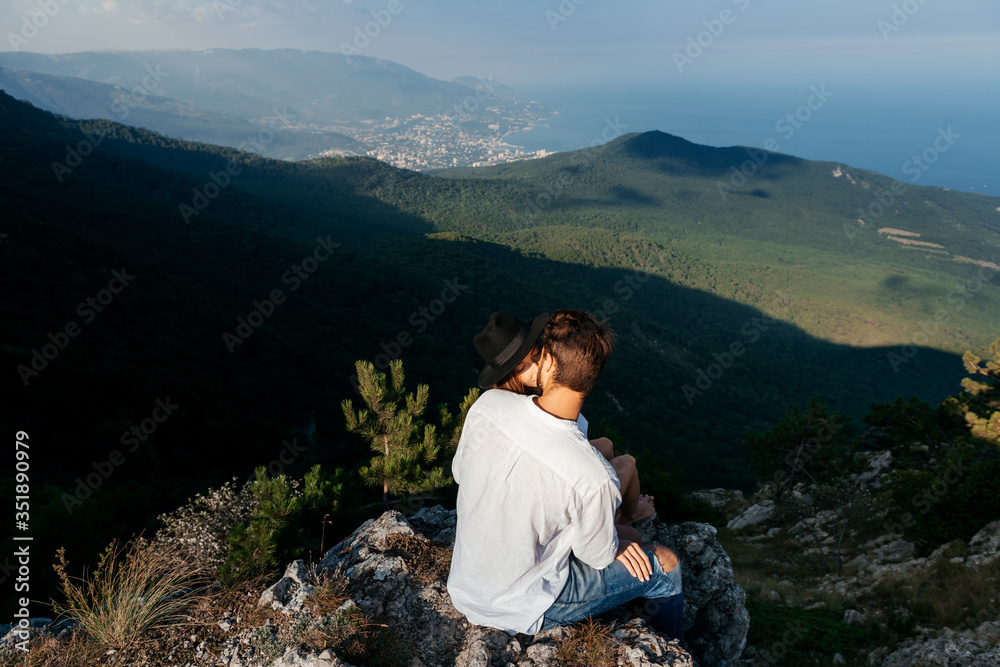 Attractive young loving couple of man in white shirt and blue jeans with girl in dress on sunny outdoor background in the green mountain landscape