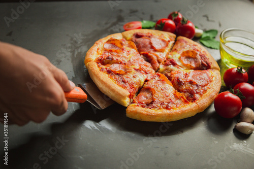Top view of hot pepperoni pizza,Tasty pepperoni pizza and cooking ingredients tomatoes basil on black background.