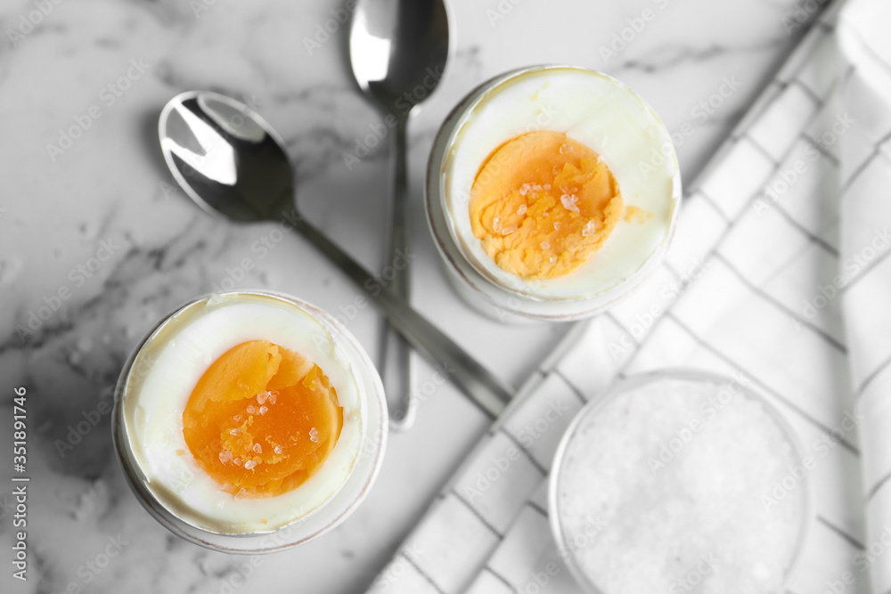 Tasty medium boiled eggs in ceramic holders on white marble table, flat lay Tasty medium boiled eggs in ceramic holders on white marble table, flat lay