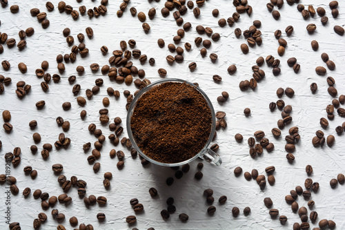 A Cup filled with coffee beans. Coffee beans are scattered on the white surface of the table