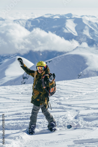 Gudauri ski resort in Georgia. Girl wih bright helment and colorful backpack on a snowboard admires snow-capped mountain peaks and clouds which hanging low overhead.  She is going to freeride.
