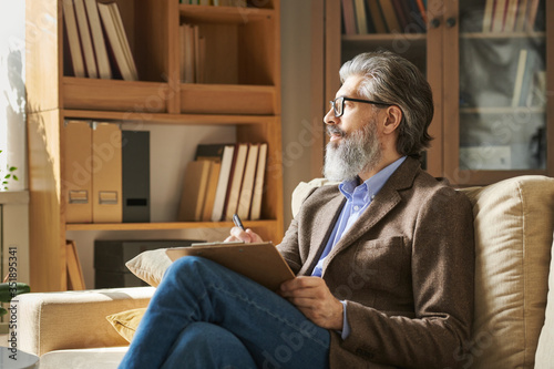 Serious aged professional with grey hair and beard sitting on couch in office