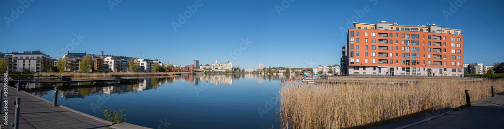 View over the bay Hammarby sjö with waterfront buildings and boats at the embarkment a sunny spring morning with water mirror reflecting in Stockholm
