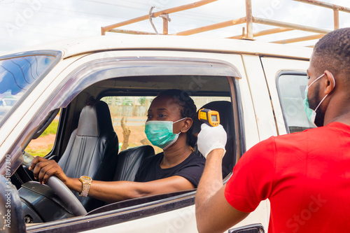 young black man wearing a nose mask, checking the temperature of a black woman driving a car