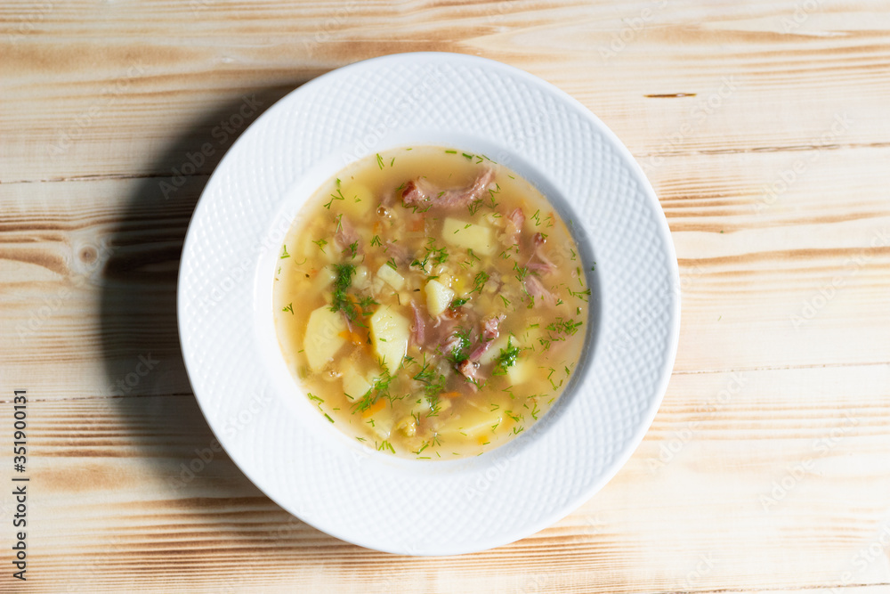 Pea soup with potato, smoked meat, spices in white plate on wooden background Pea soup with potato, smoked meat, spices in white plate on wooden background