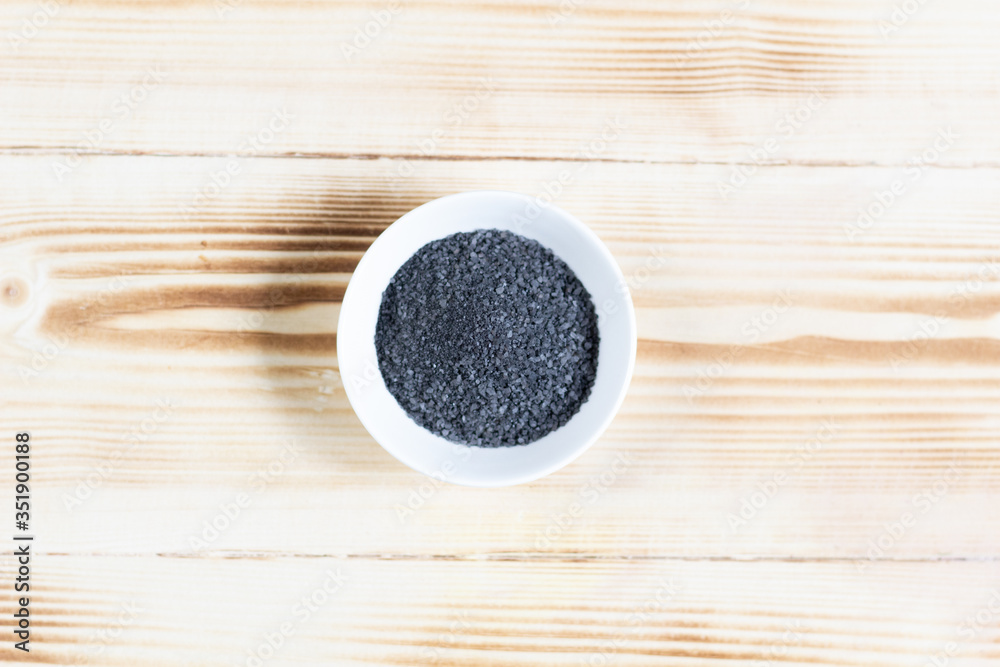 Flat lay on black (burned with powder) salt in white bowl on wooden background Flat lay on black (burned with powder) salt in white bowl on wooden background