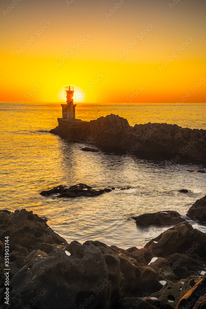 Detail of the sun behind the lighthouse in the orange sunset of the town of Pasajes San Juan. Gipuzkoa, Basque Country. Vertical photo