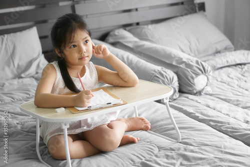 asian child new idea think or kid girl smile writing drawing and enjoy doing homework or happy learn and training write on paper with table by stay home and kindergarten study online on gray bed room