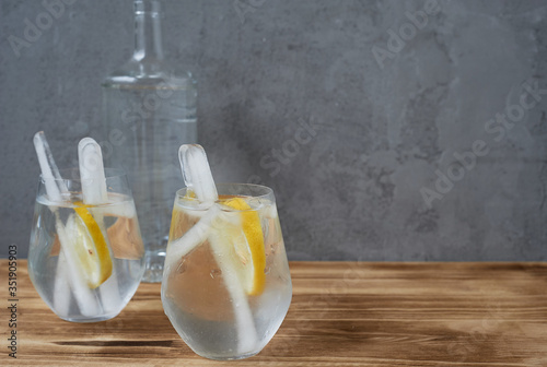 Water with lemon.Refreshing. In transparent glasses, with long ice sticks. Concrete and wood.