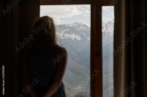 Blurred silhouette of a girl who watches the mountain landscape outside the window. Snow-capped peaks and green forests of the Caucasus Mountains.